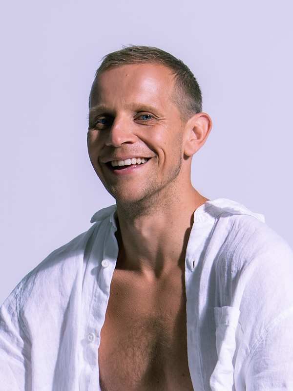 Escort Mann Anado von haut-nah.org mit freiem Oberkörper sitzt, lachend