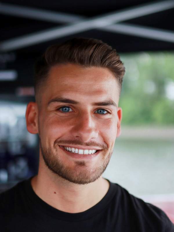 Escort Mann Niclas von haut-nah.org im schwarzen Shirt lächelt geradeaus
