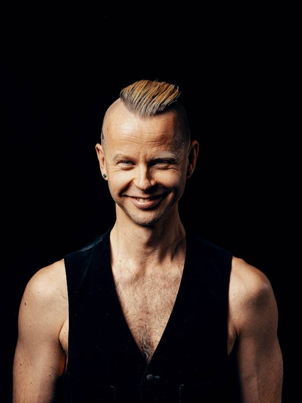 Callboy Mann Tom von haut-nah.org mit schwarzer Weste und freien Oberkoerper, lächelt