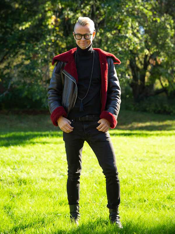 Escort Mann Tom von haut-nah.org, Ganzkörper, mit schwarzer Lederjacke mit roten Bund steht im Park
