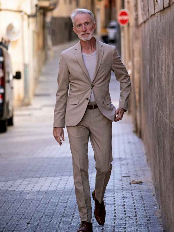 Callboy Robert von haut-nah.org laeuft durch spanische Altstadt mit beigen Anzug, seriöser Blick