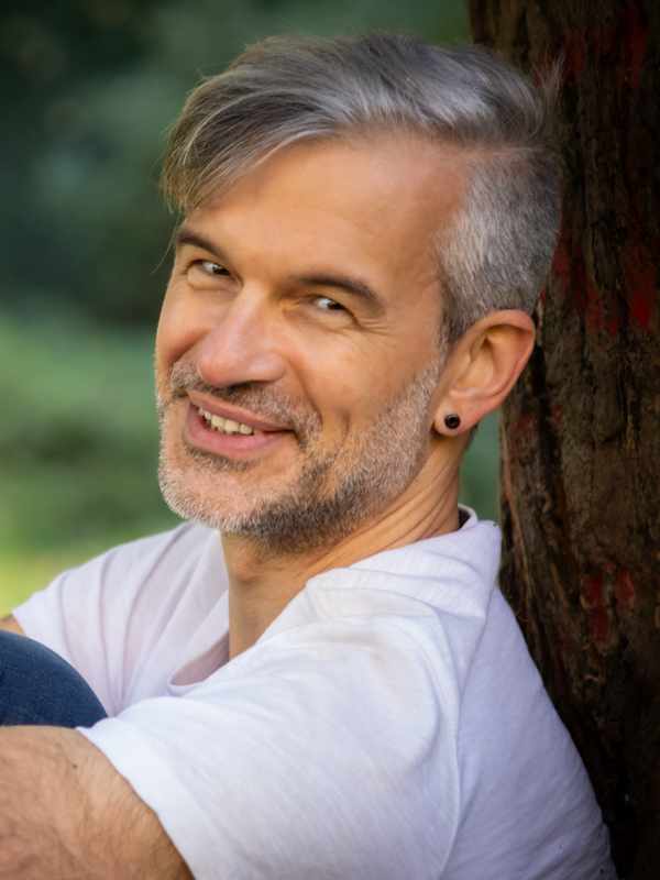 Callboy Roman von haut-nah.org im Sitzen am Baum gelehnt, Kopf zur Seite, lächelnd