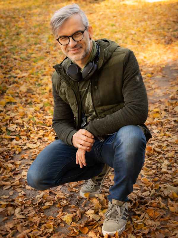 Callboy Roman von haut-nah.org in der Hocke im Laub, im Freizeitlook, lächelnd