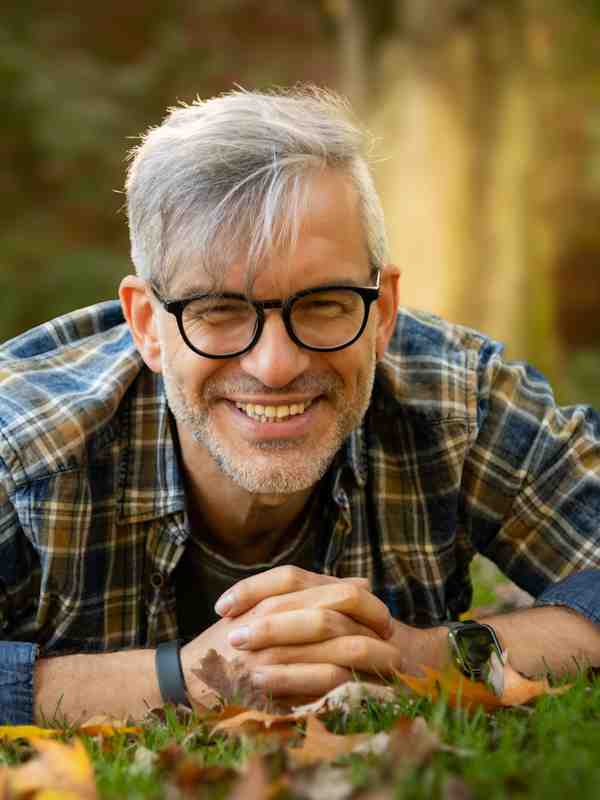 Escort Mann Roman von haut-nah.org liegt in grüner Wiese mit blau karierten Hemd, lächelnd