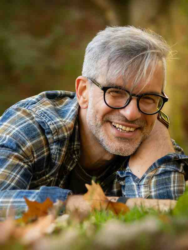 Escort Mann Roman von haut-nah.org liegt in grüner Wiese mit blau karierten Hemd, lächelnd