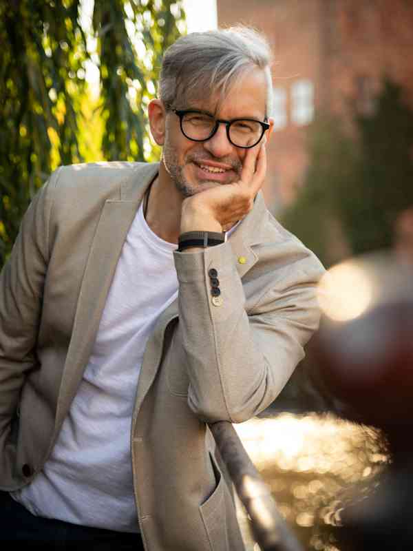 Male Escort Roman from haut-nah.org with beige jacket, child leaning on hand, smiling