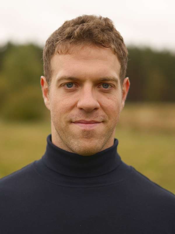 Escort Mann Simon von haut-nah.org vor Wiese lächelt geradeaus