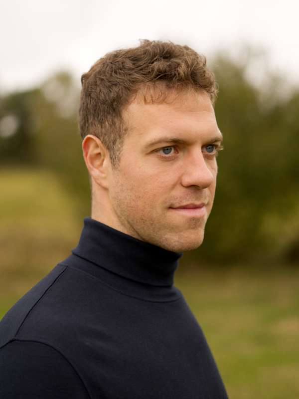 Escort Mann Simon von haut-nah.org vor Wiese lächelt seitlich