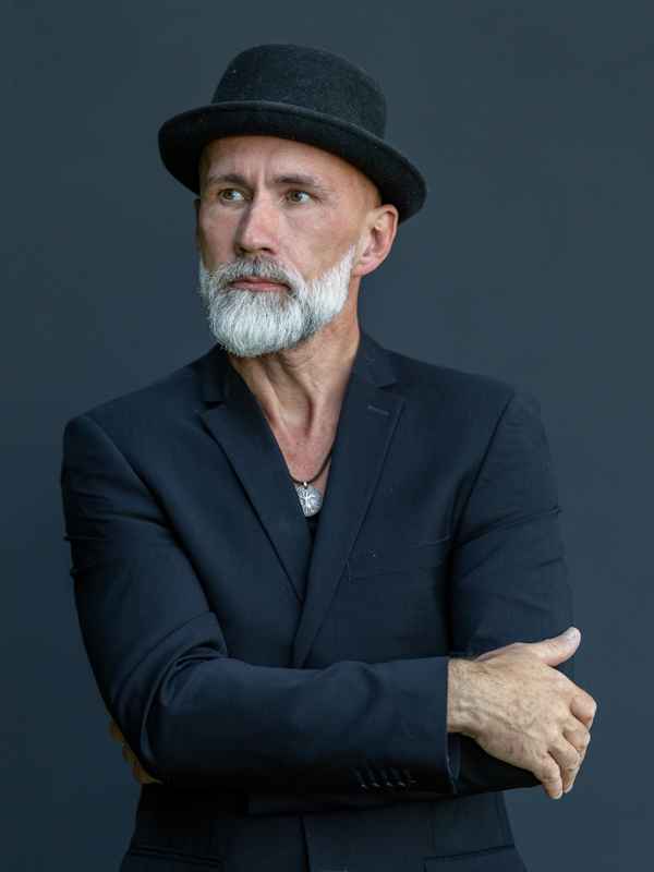 Callboy Leon von haut-nah.org elegant schwarz gekleidet mit Hut, Hände ineinander verschränkt