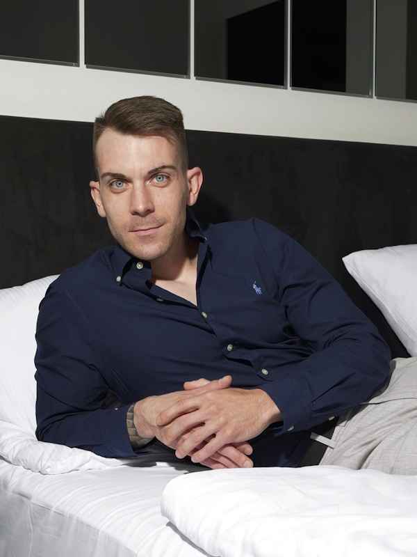 Escort Mann Dennis von haut-nah.org im blauen Hemd liegt auf dem Bett