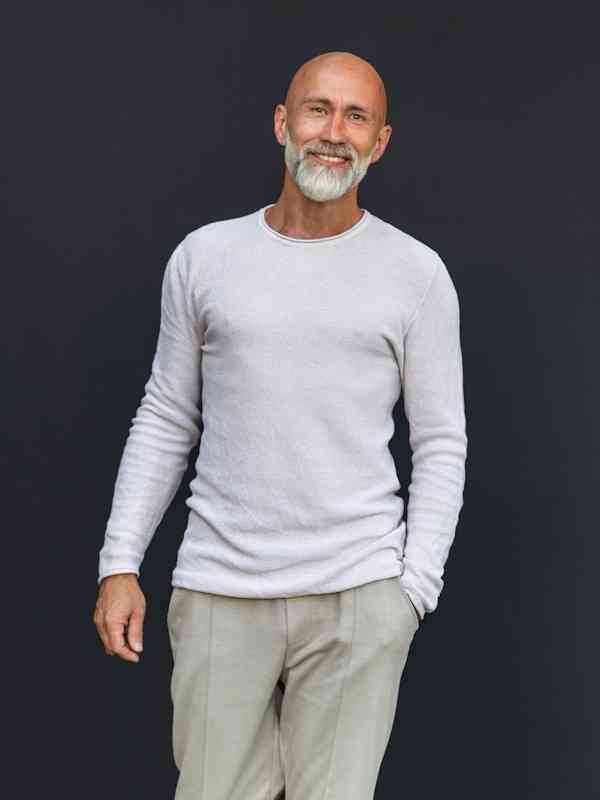 Escort-Mann Leon von haut-nah.org im weissgrauen Pullover laechelnd