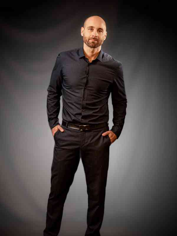 Escort Mann William von haut-nah.org im Stehen, Hände locker in den Taschen, im schwarzen Dress