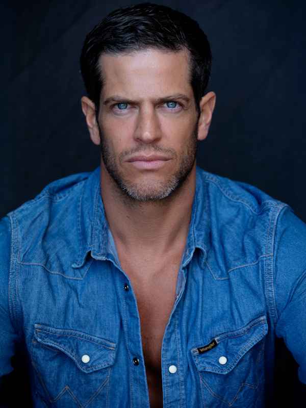 Callboy Chris von haut-nah.org im blauen Jeanshemd im Sitzen, verführerischer Blick geradeaus