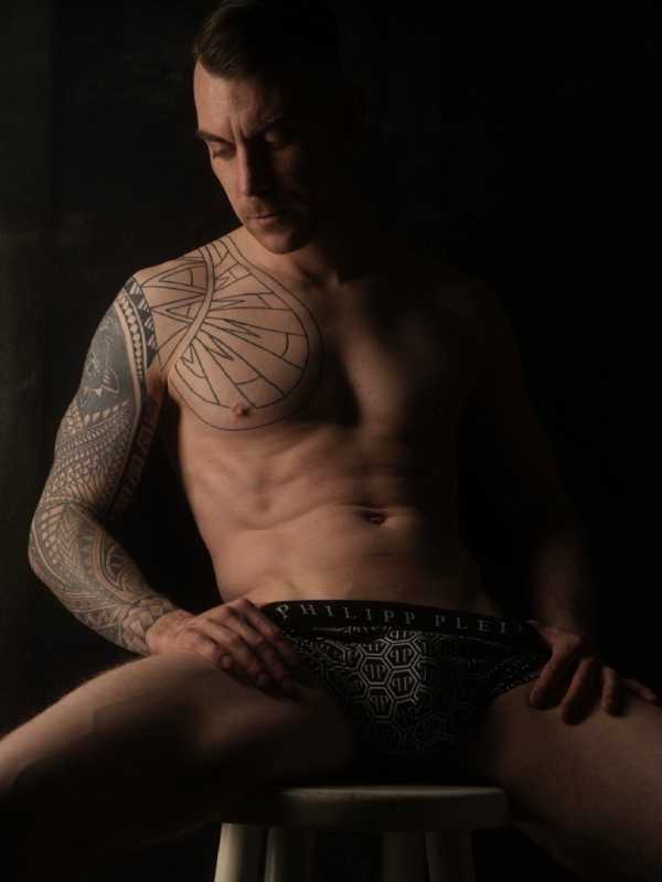 Callboy Dennis von haut-nah.org mit freien Oberkörper und Tattoo im Sitzen