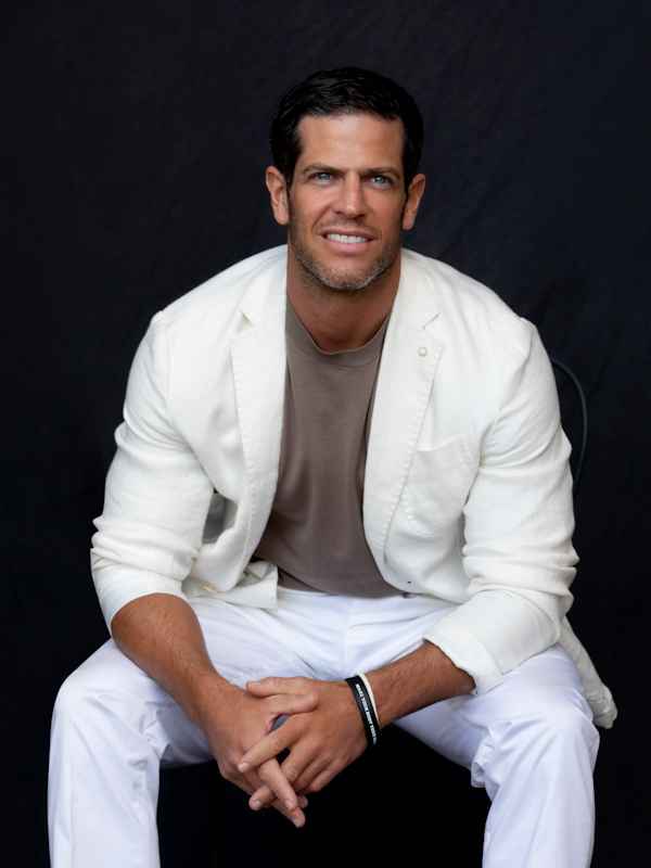 Male Escort Chris from haut-nah.org fashionably relaxed with white dress in sitting smiles easily