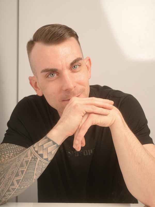 Escort Mann Dennis von haut-nah.org Hände auf Tisch aufgelehnt, lächelt