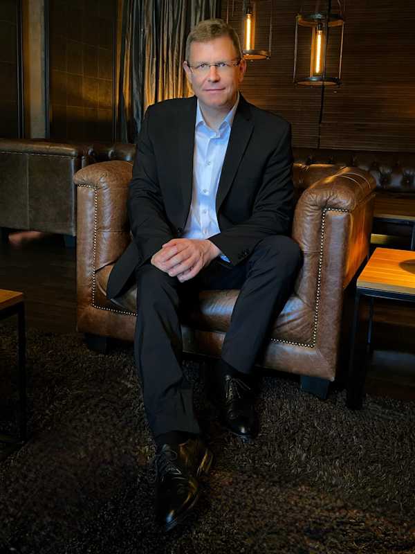 Callboy Alexander von haut-nah.org im Anzug auf Ledersessel lächelt leicht