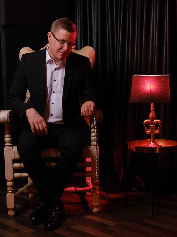 Callboy Alexander von haut-nah.org im Anzug auf Stuhl, gesenkter Blick