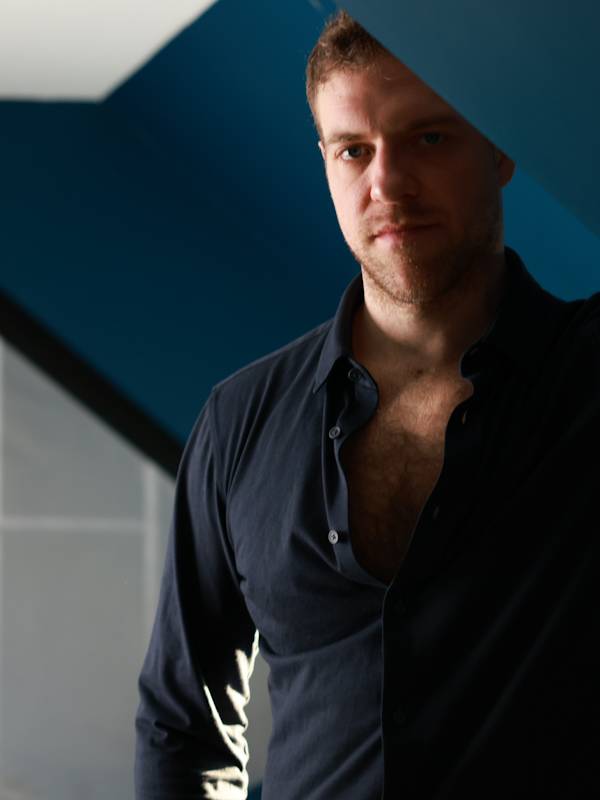 Callboy Simon von haut-nah.org im blauen Hemd, angelehnt an Dachschräge