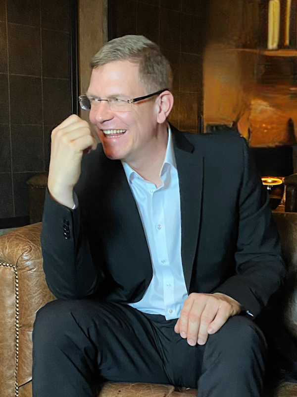 Callboy Alexander von haut-nah.org im Anzug auf Ledersessel lacht