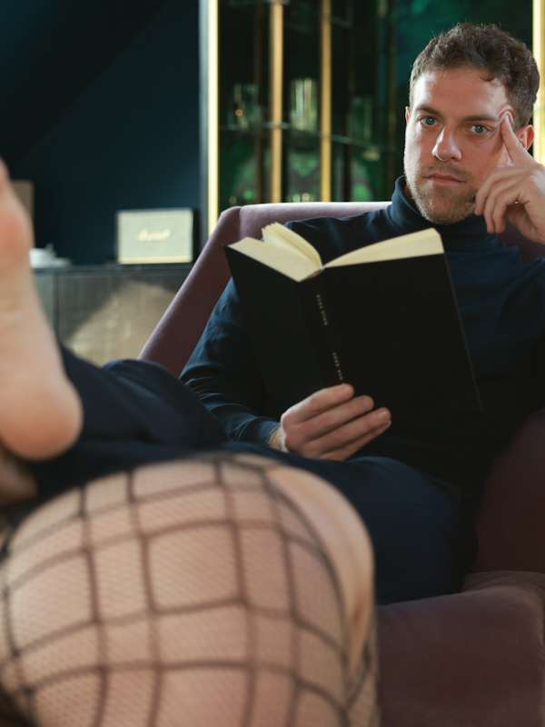 Escort Mann Simon von haut-nah.org Füsse auf dem Rücken einer Frau, liest Buch dabei