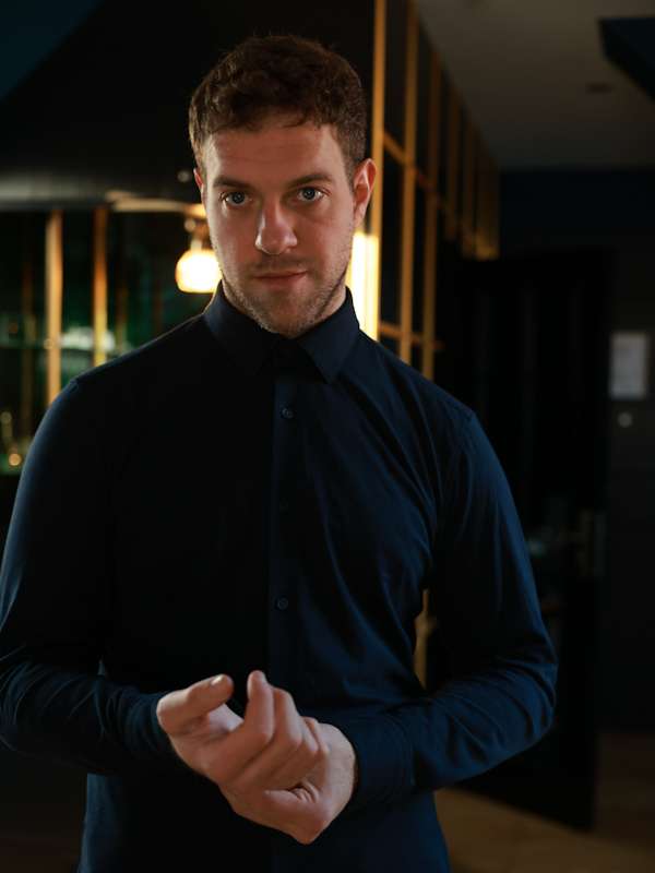 Escort Mann Simon von haut-nah.org knöpft Ärmel vom blauem Hemd zu