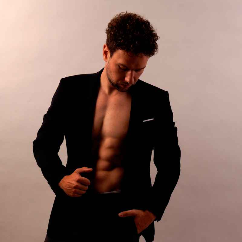 Male Escort Julian from haut-nah.org in a black blazer, bare-chested, medium shot