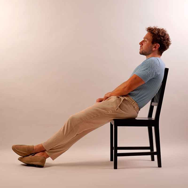 Male Escort Julian from haut-nah.org, sitting sideways on a chair in a blue shirt, body shot