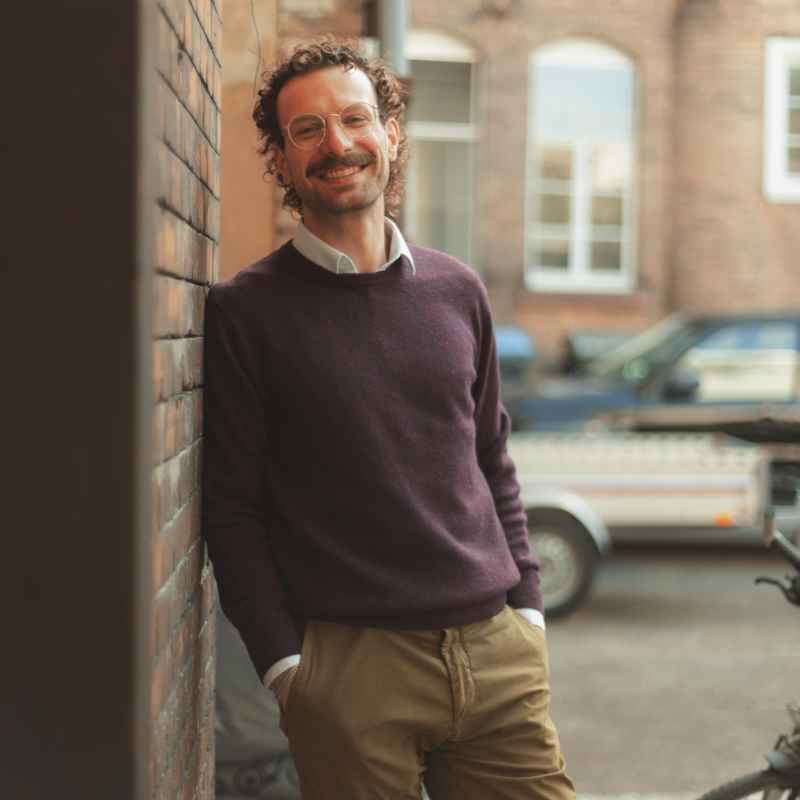 Callboy Malte von haut-nah.org mit lila Pullover lässig stehend an einer Wand